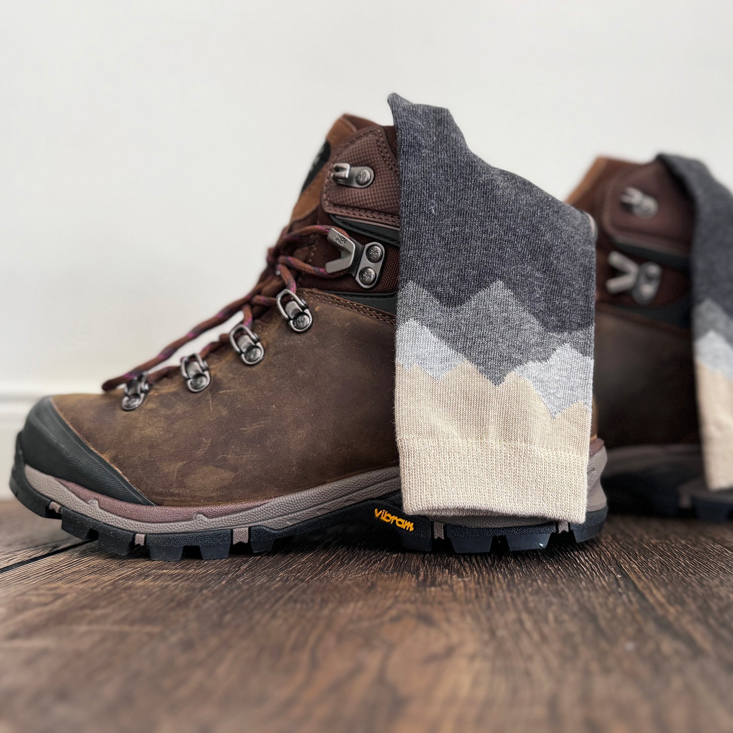 Brown hiking boots with gray mountain-patterned socks on a wooden floor.