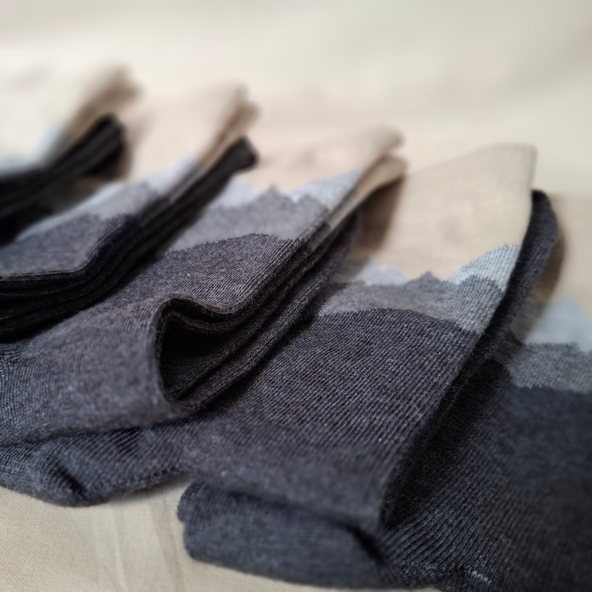Stack of gray socks with mountain pattern on a beige surface.