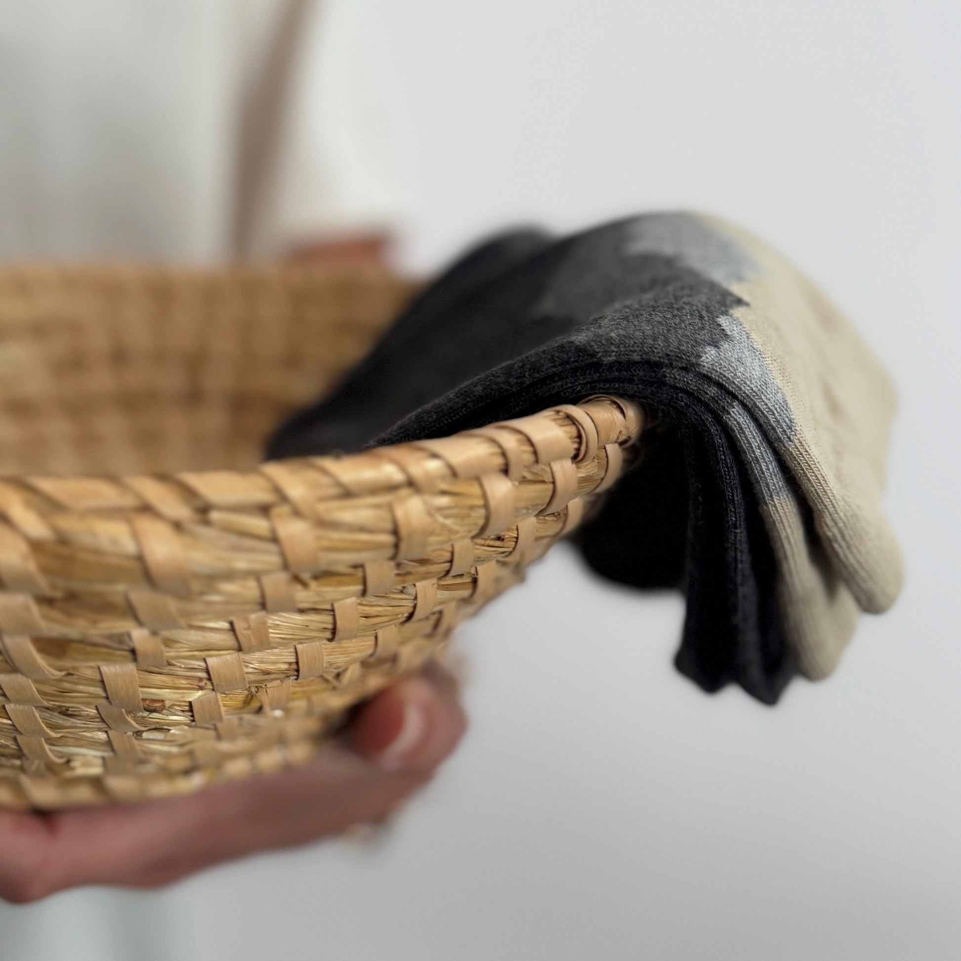 Person holding a woven basket with folded cotton socks inside on a white background.