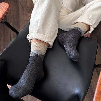 Person wearing dark gray  crew socks sitting on a black chair with a wooden floor.