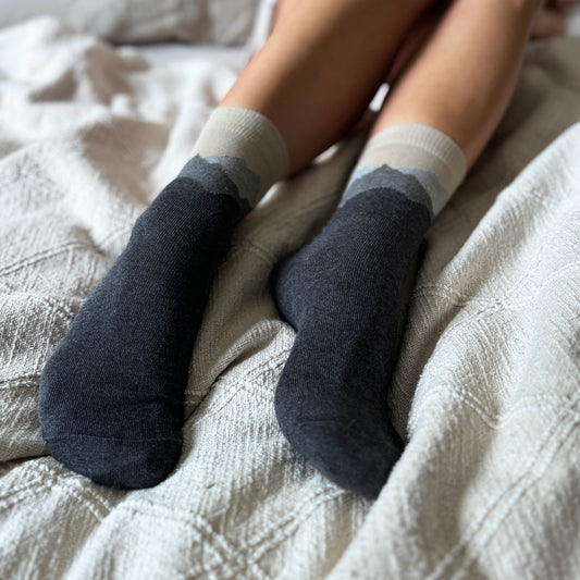 Person wearing dark gray cotton socks with mountain aerial perspective of Julian Alps on a light beige blanket.